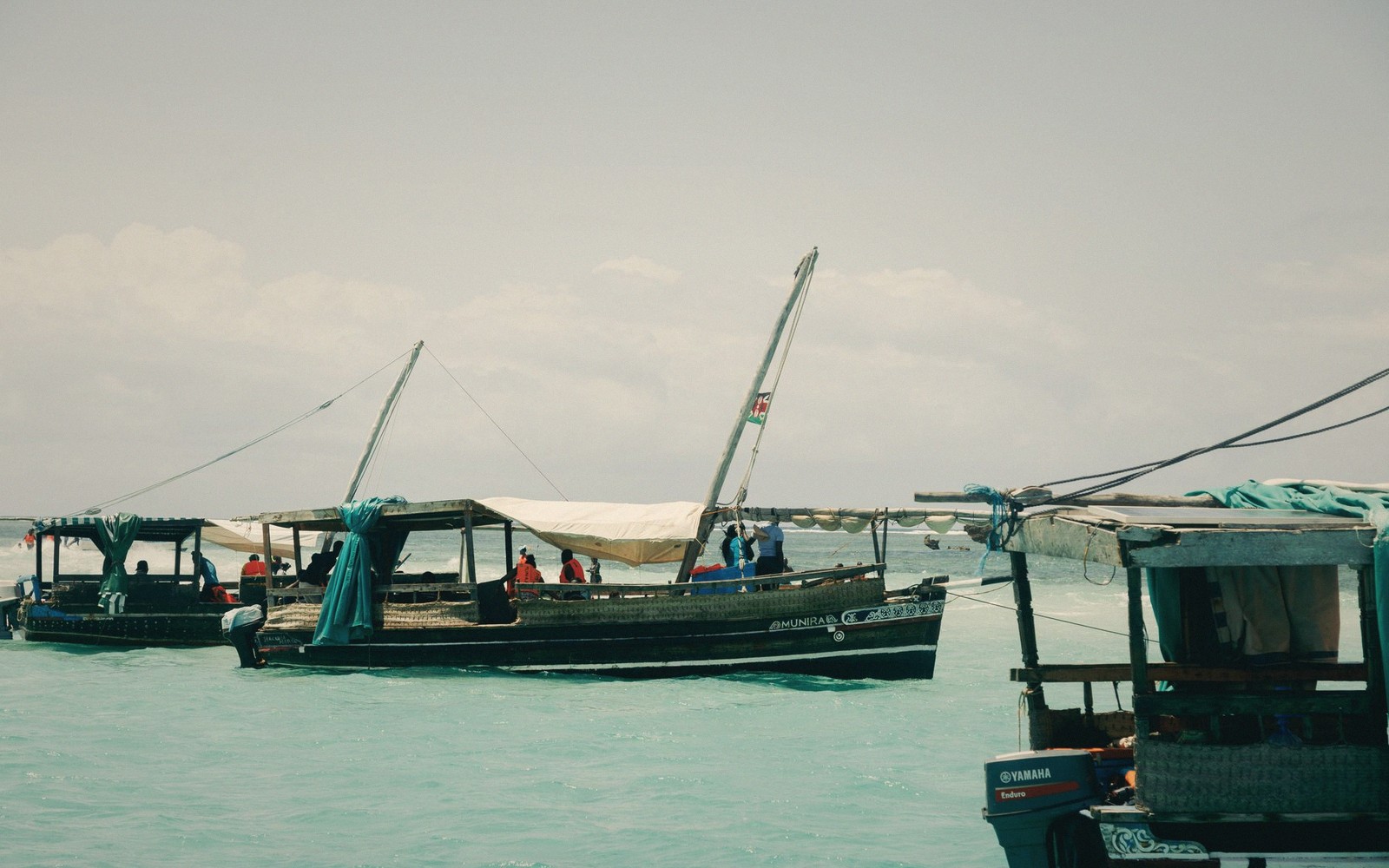 Wooden dhows with canopies carry passengers on turquoise coastal waters near Mombasa